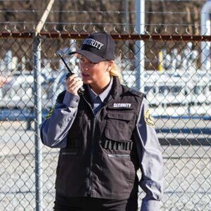 Security guard standing in front of chain link fence, talking into a radio