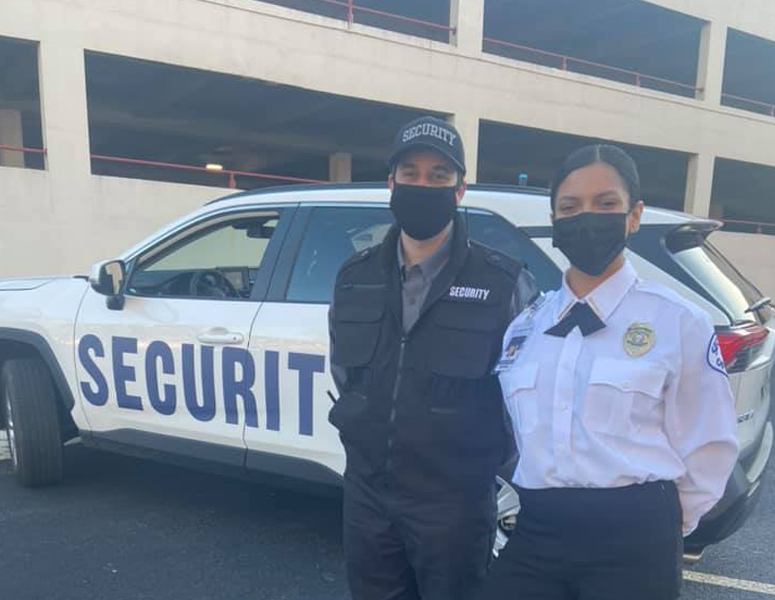 Two security guards standing beside a security patrol vehicle parked outside a parking garage