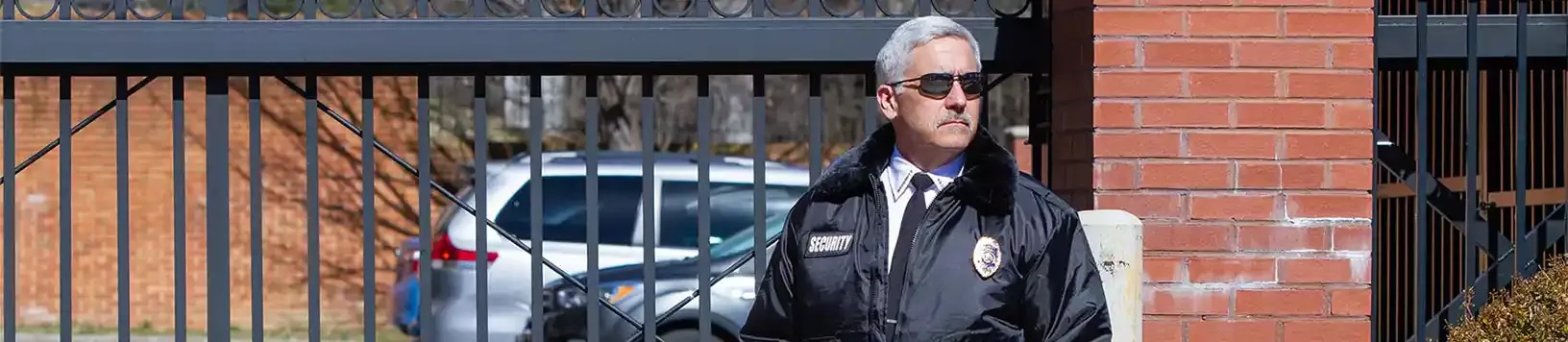 Security guard on a security patrol, wearing jacket in front of gated parking lot area