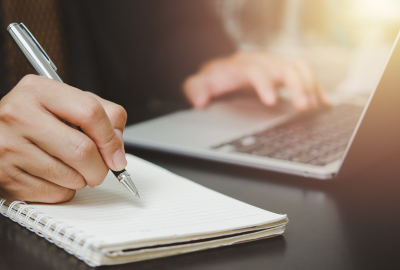 Person writing on notepad and typing on computer