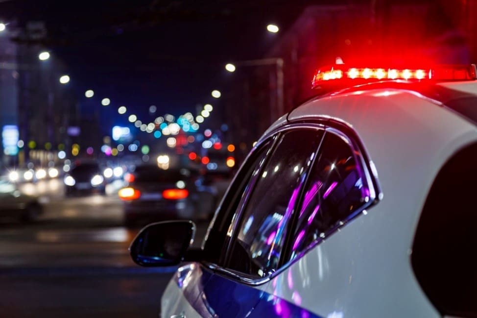 A police vehicle with flashing red lights is parked on a busy city street at night.