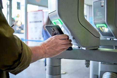 A person scans a mobile device at security with a green light indicator, suggesting biometric or mobile credential access control.