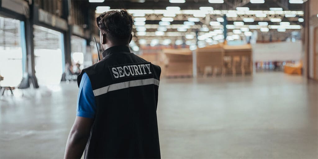 Security guard wearing a vest labeled ‘SECURITY’ patrols a large warehouse