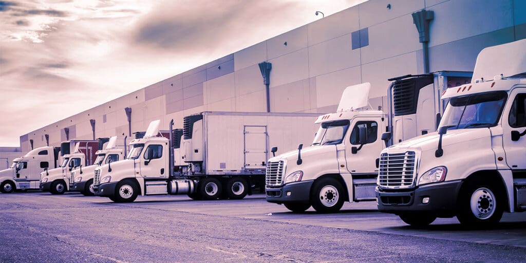 Row of white semi-trucks parked outside a large warehouse distribution center