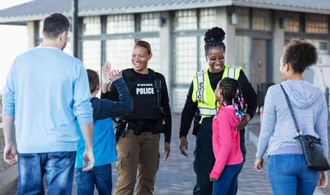two off duty law enforcement officers in uniform smiling and high fiving children